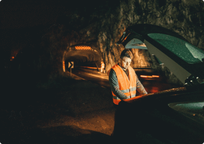 Man in safety vest inspecting car at night.