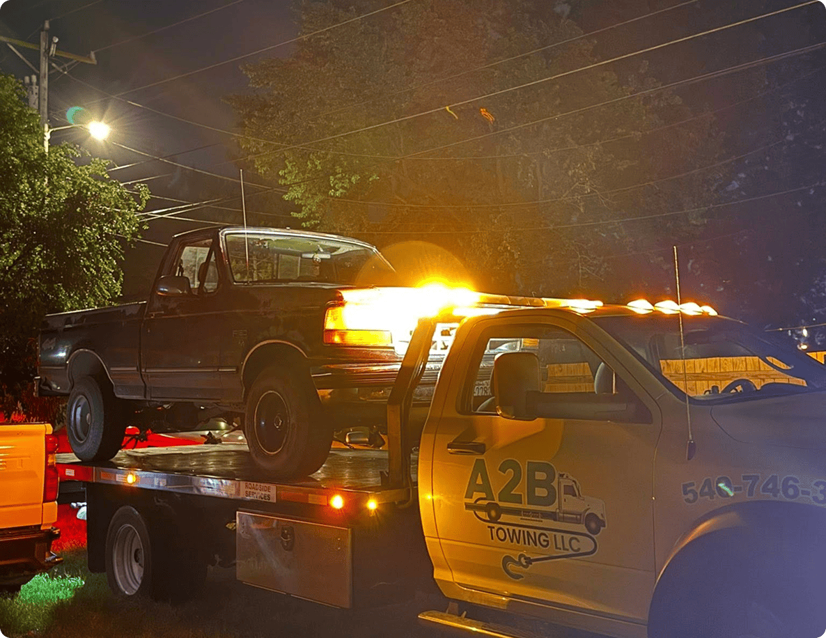 Tow truck transporting a pickup truck at night.