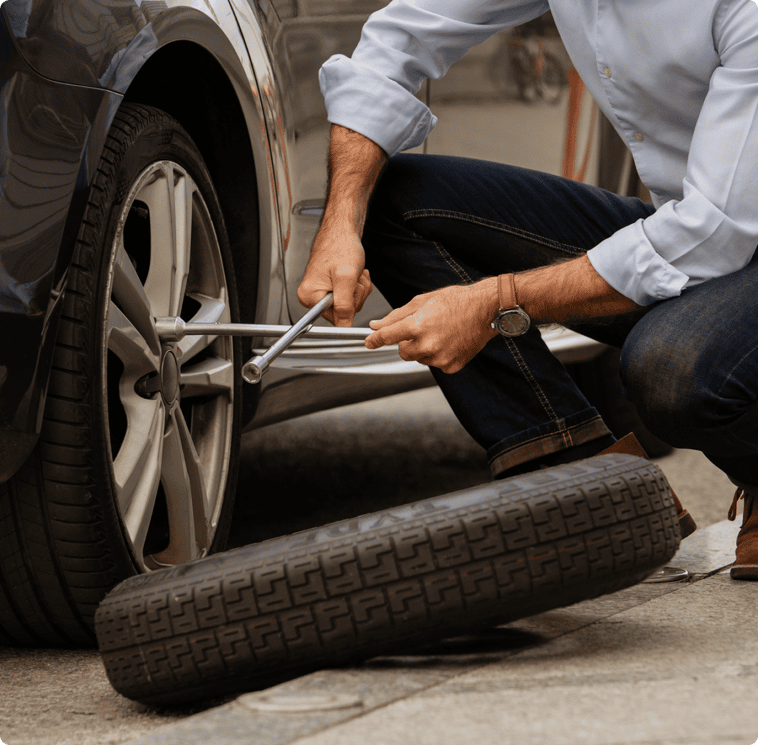 Person changing a car tire outdoors.